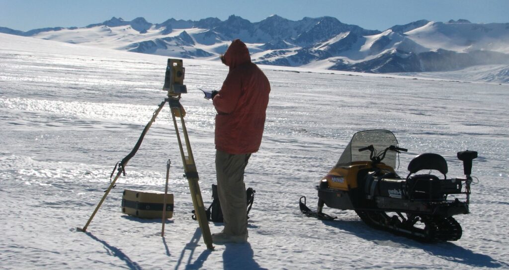 Surveyor in icy area with snow mobile and measuring equipment
