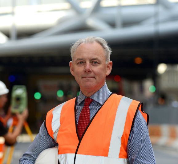 Image shows Surveyor stood infront of construction of stadium or arena.